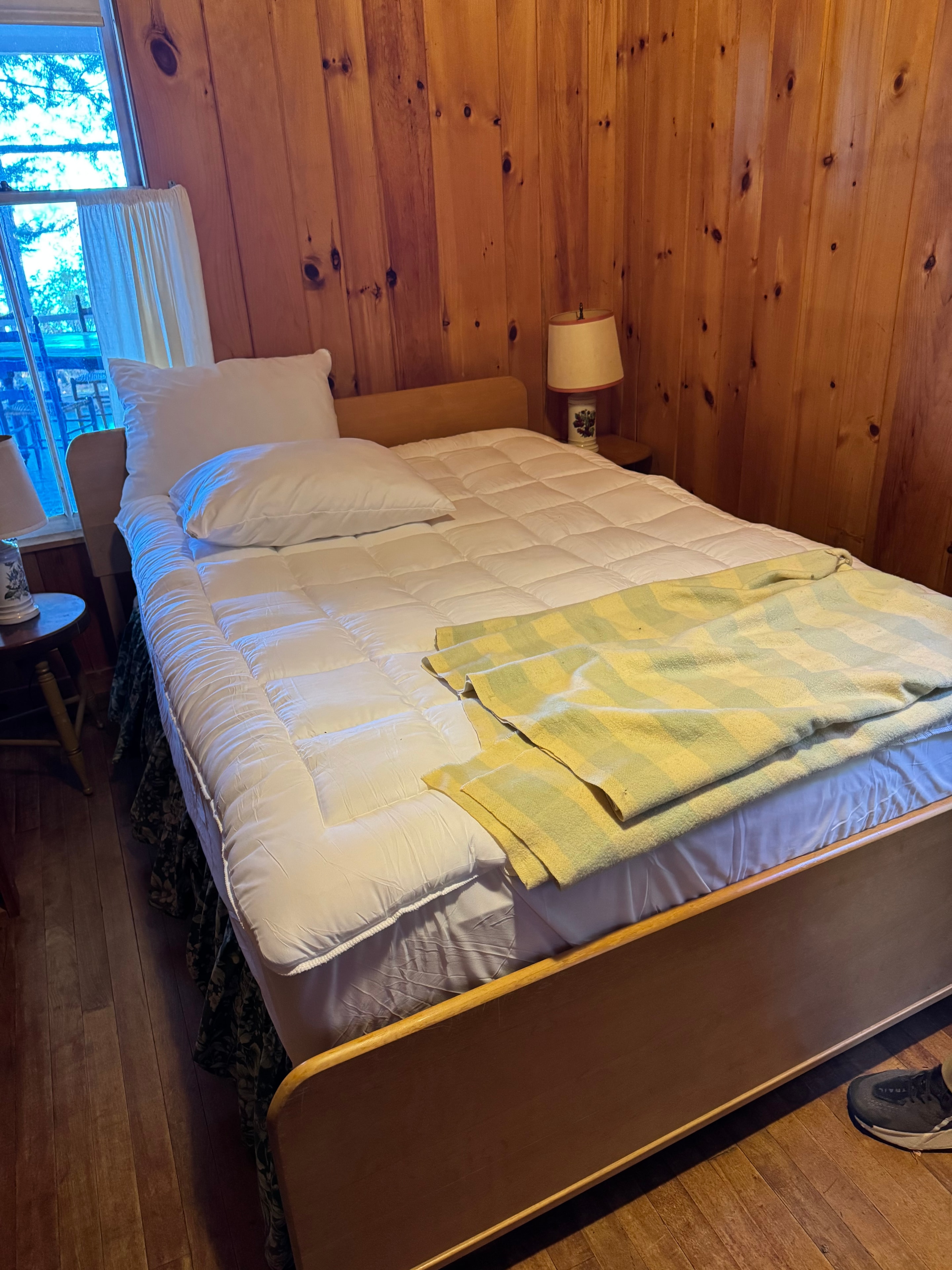 Lake camp bedroom before staging — unmade bed with yellow towel on wood ceiling cabin