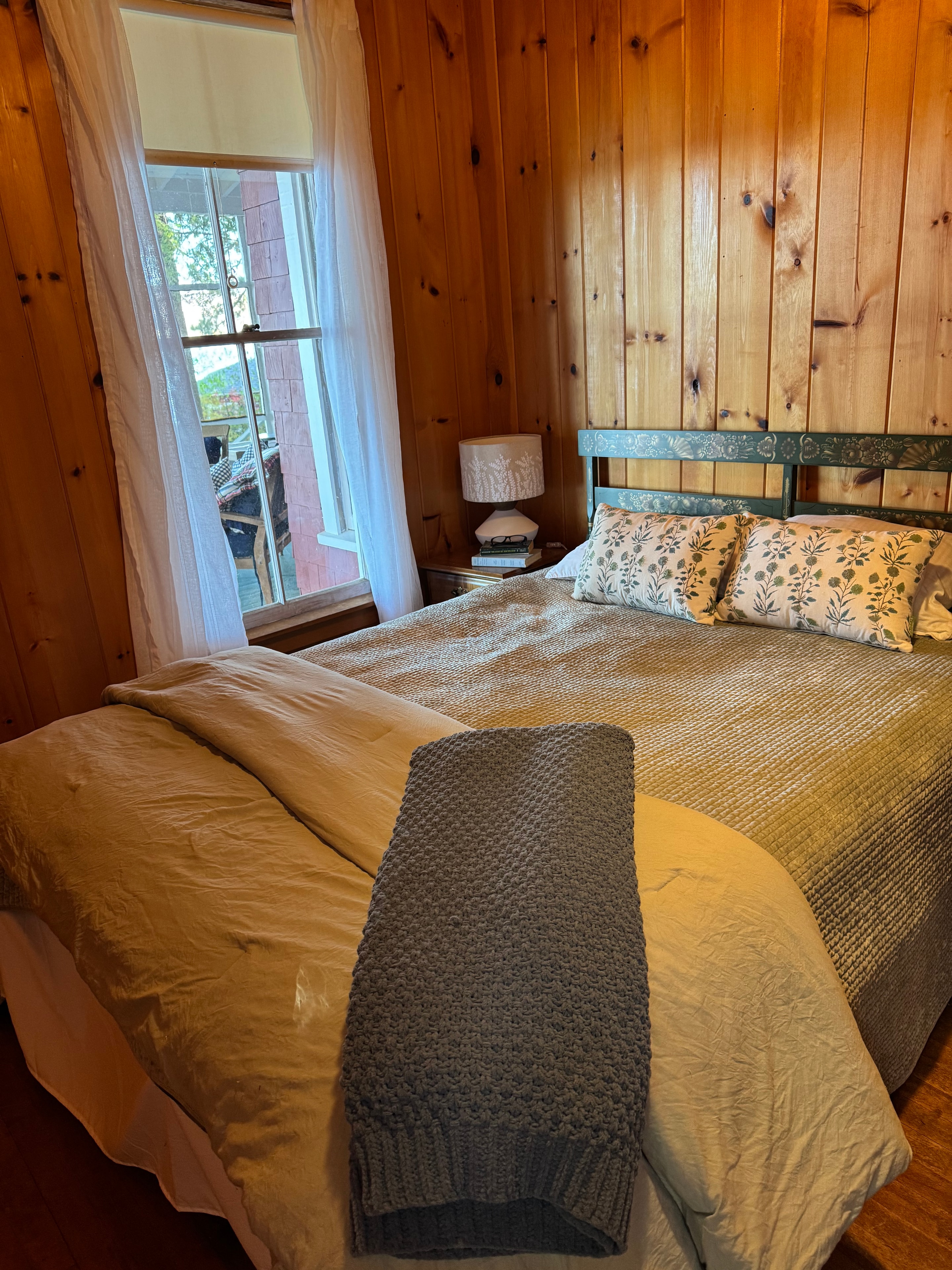Lake camp bedroom after staging — styled bed with floral pillows and grey knit throw