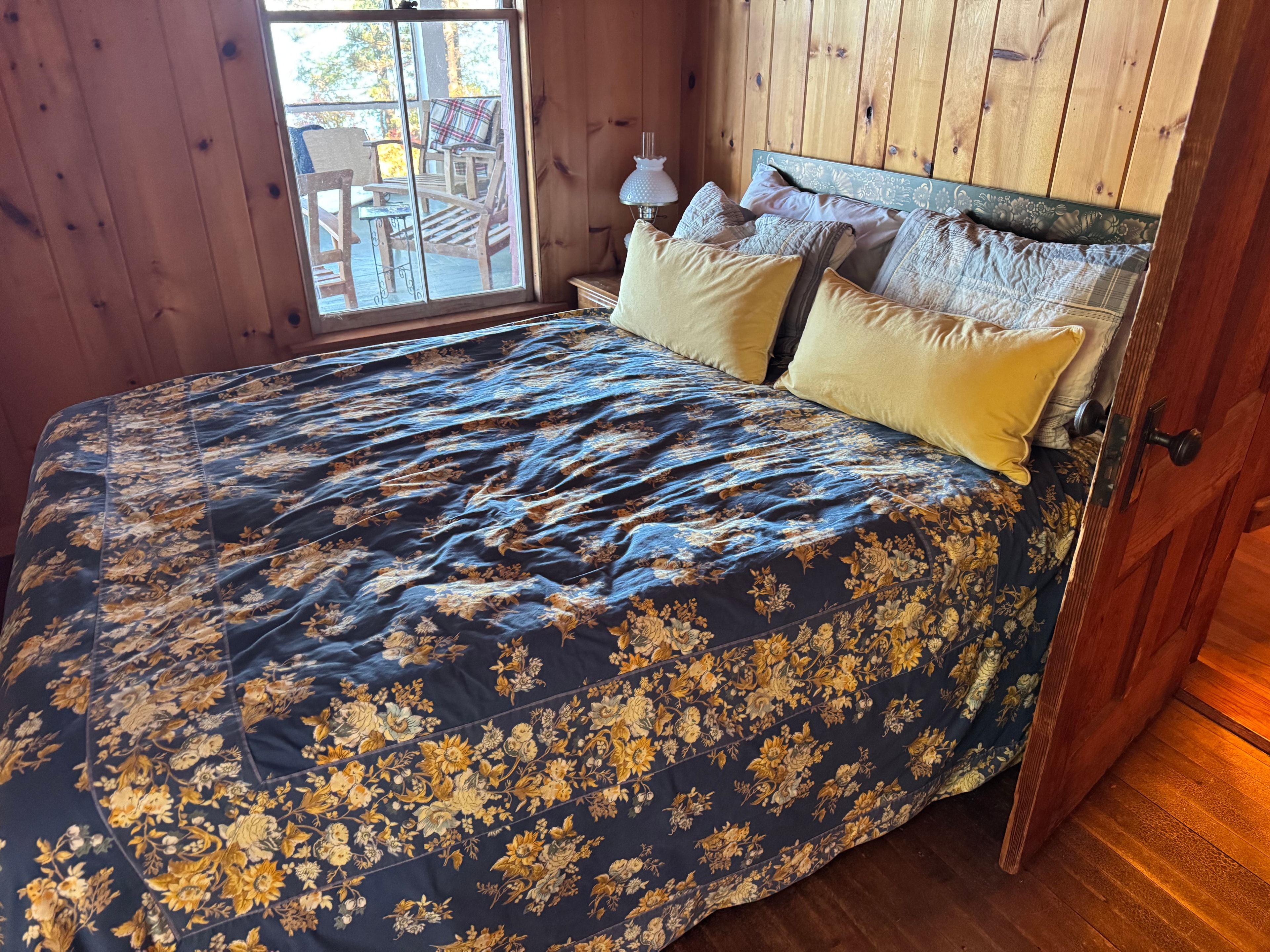 Lake camp bedroom before staging — navy and gold floral comforter on unmade bed