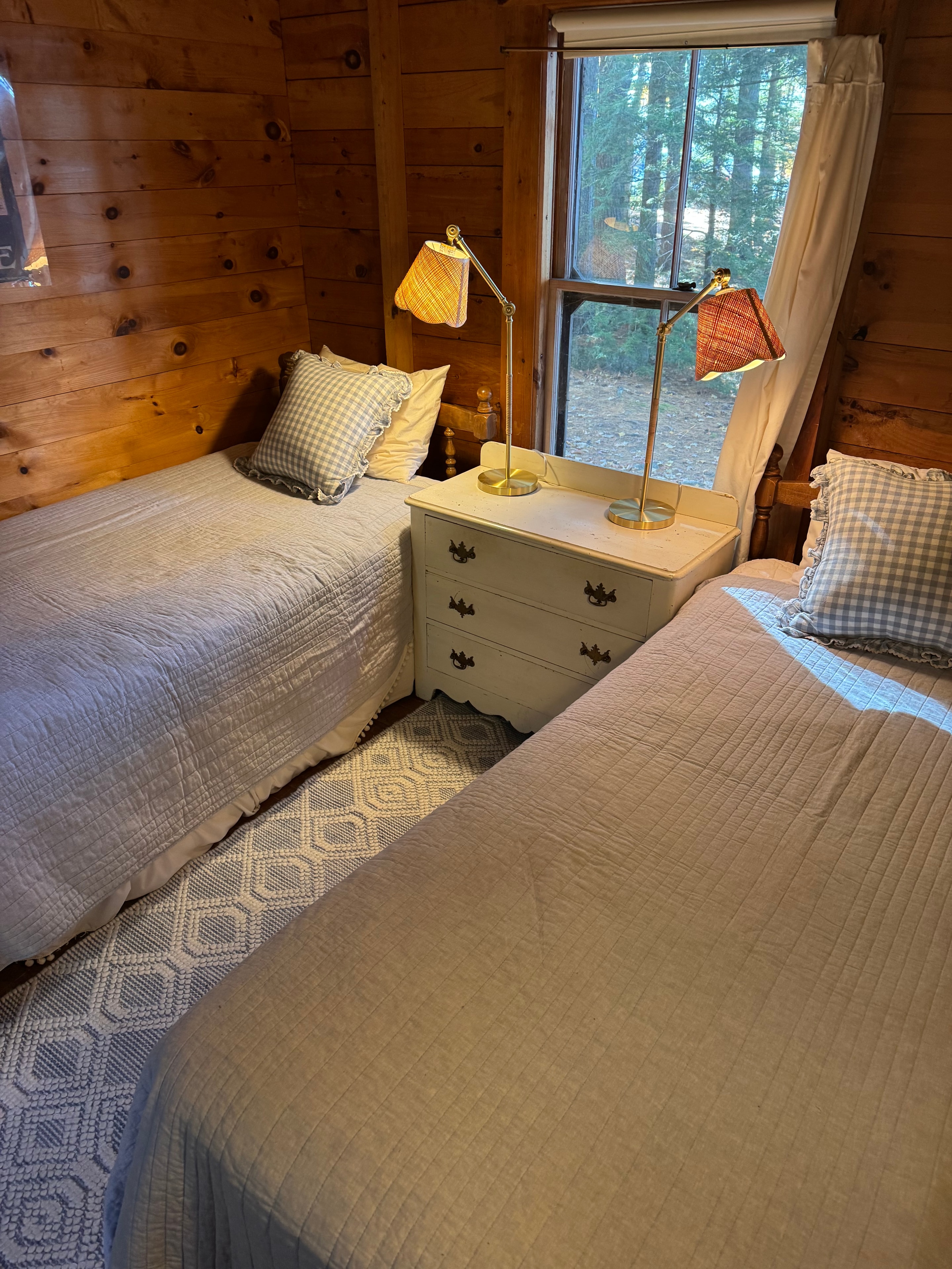 Lake camp bedroom after staging — cozy twin beds with gingham pillows and warm lamp light